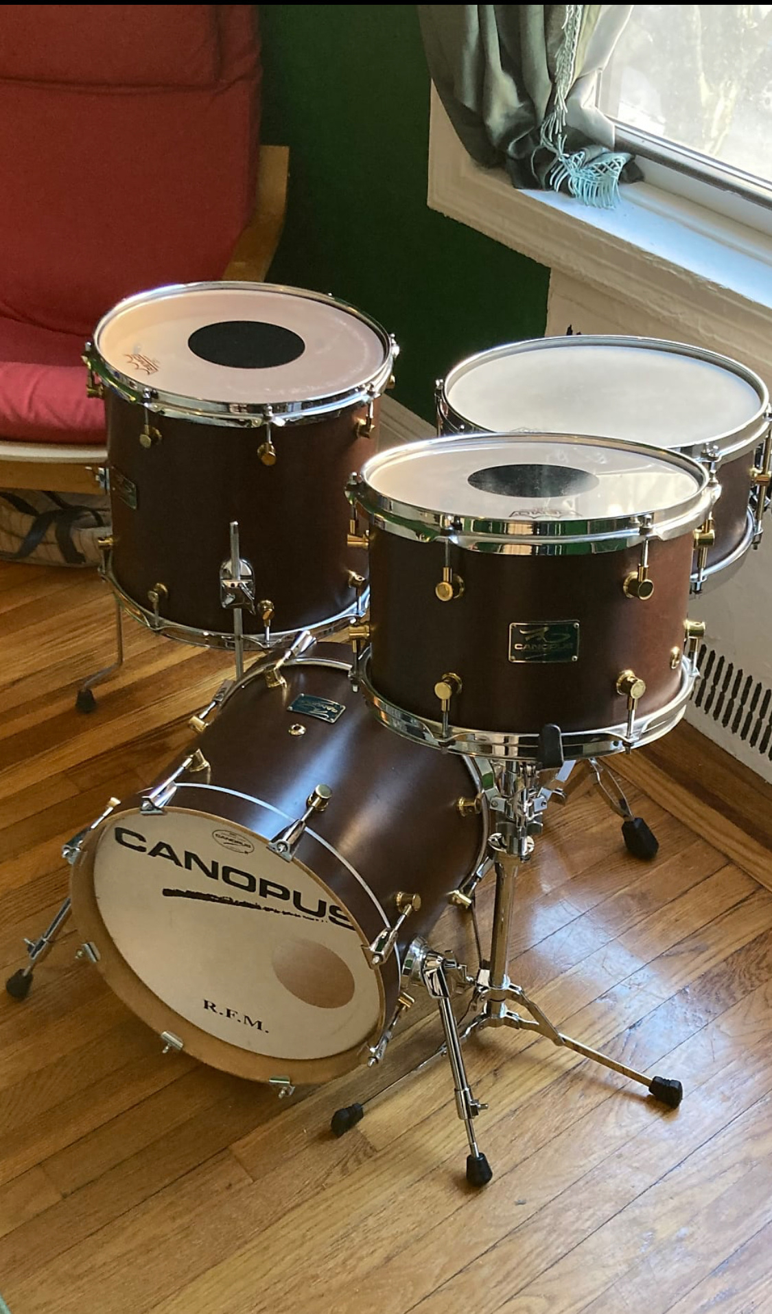 A drum set with a bass drum, two tom-toms, and a floor tom is setup in a room with hardwood floors.