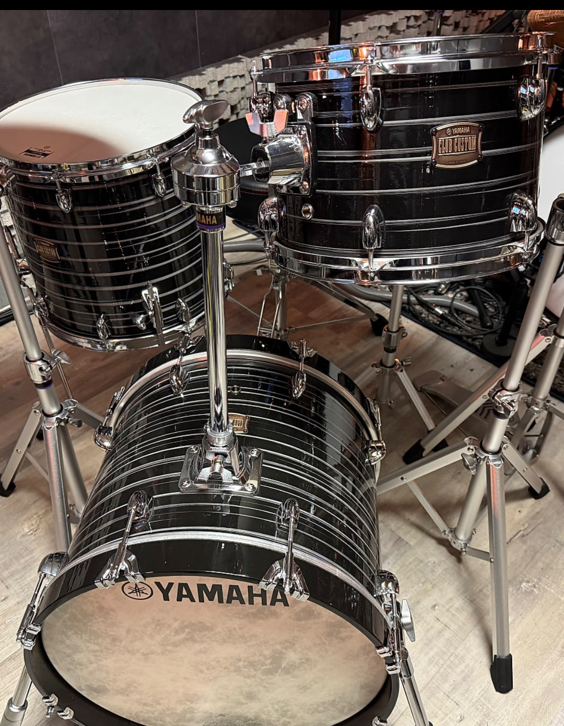 A black Yamaha drum set with chrome hardware is arranged on a wooden floor.