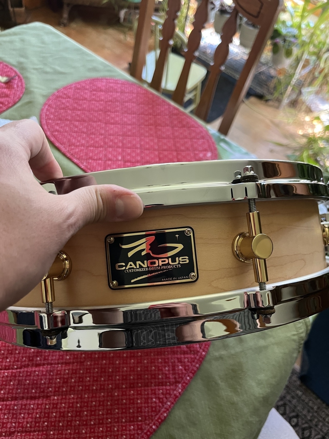 A hand is holding a Canopus snare drum above a table with red placemats.