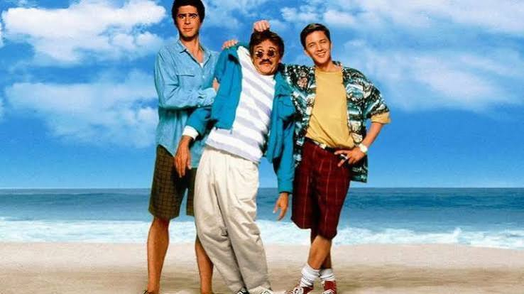 Weekend at Bernie's movie poster/promo. Three men are standing on a beach with a clear blue sky and ocean in the background, posing in casual 1980s-style clothing.